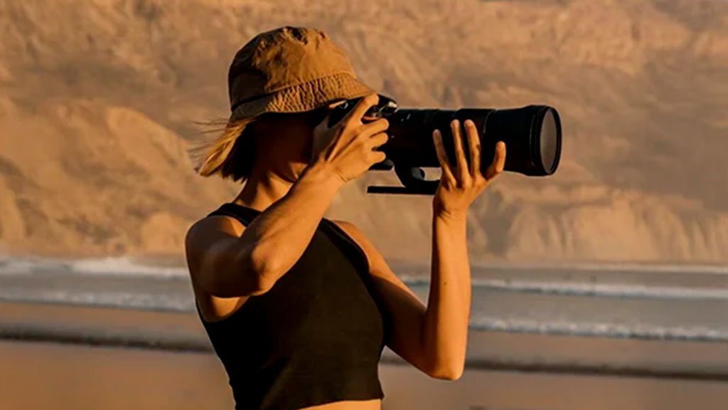 Surf Photographer A female surf photographer standing at the shoreline taking action shots of surfers in the ocean with her camera.