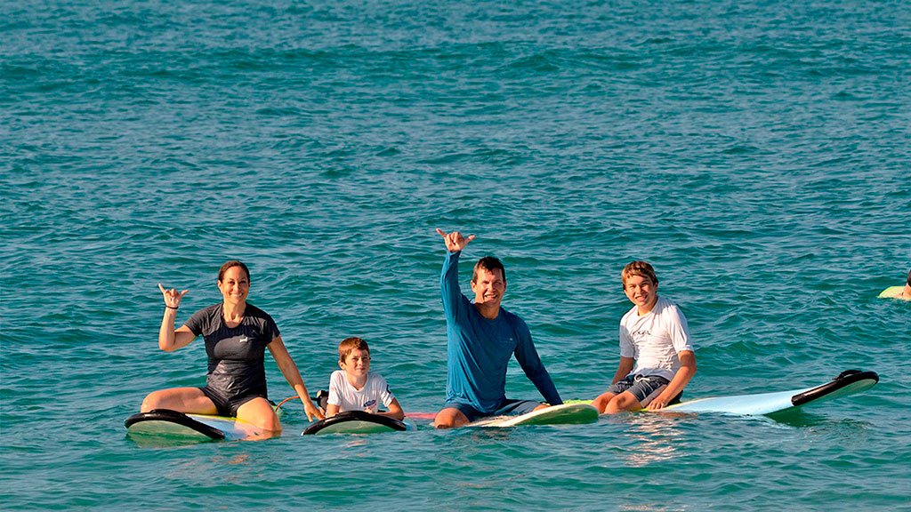 Surf Photographer A happy family sitting on their surfboards in the ocean, smiling and posing for a group photo during a WildMex surf lesson.