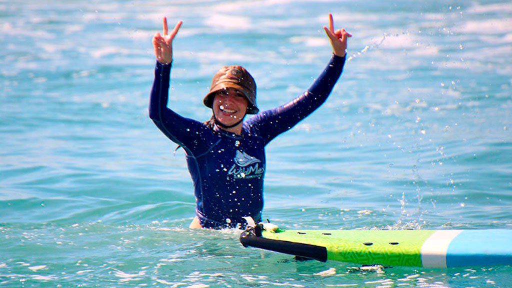 Surf Photographer A female guest in the ocean raising her hands and celebrating, smiling directly at the surf photographer after surfing a wave.